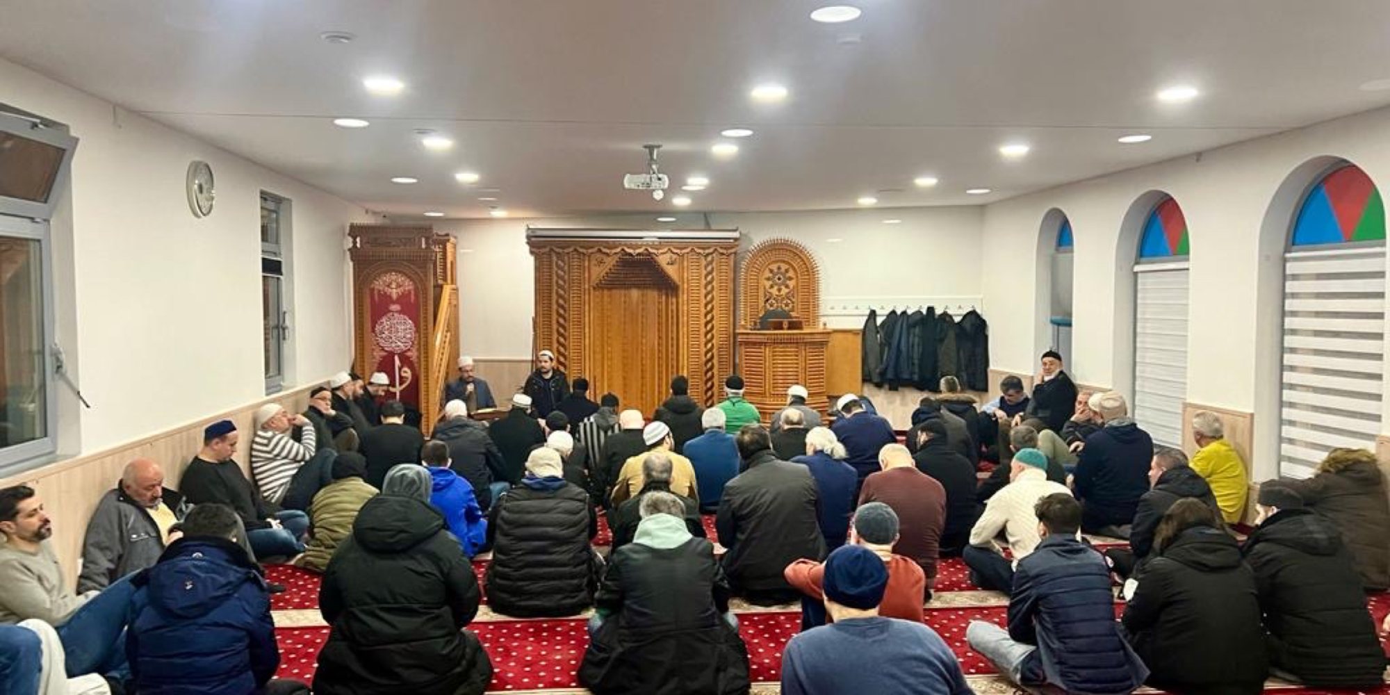 Gemeinde beim Gebet in einer Moschee mit hölzerner Minbar, von hinten aufgenommen