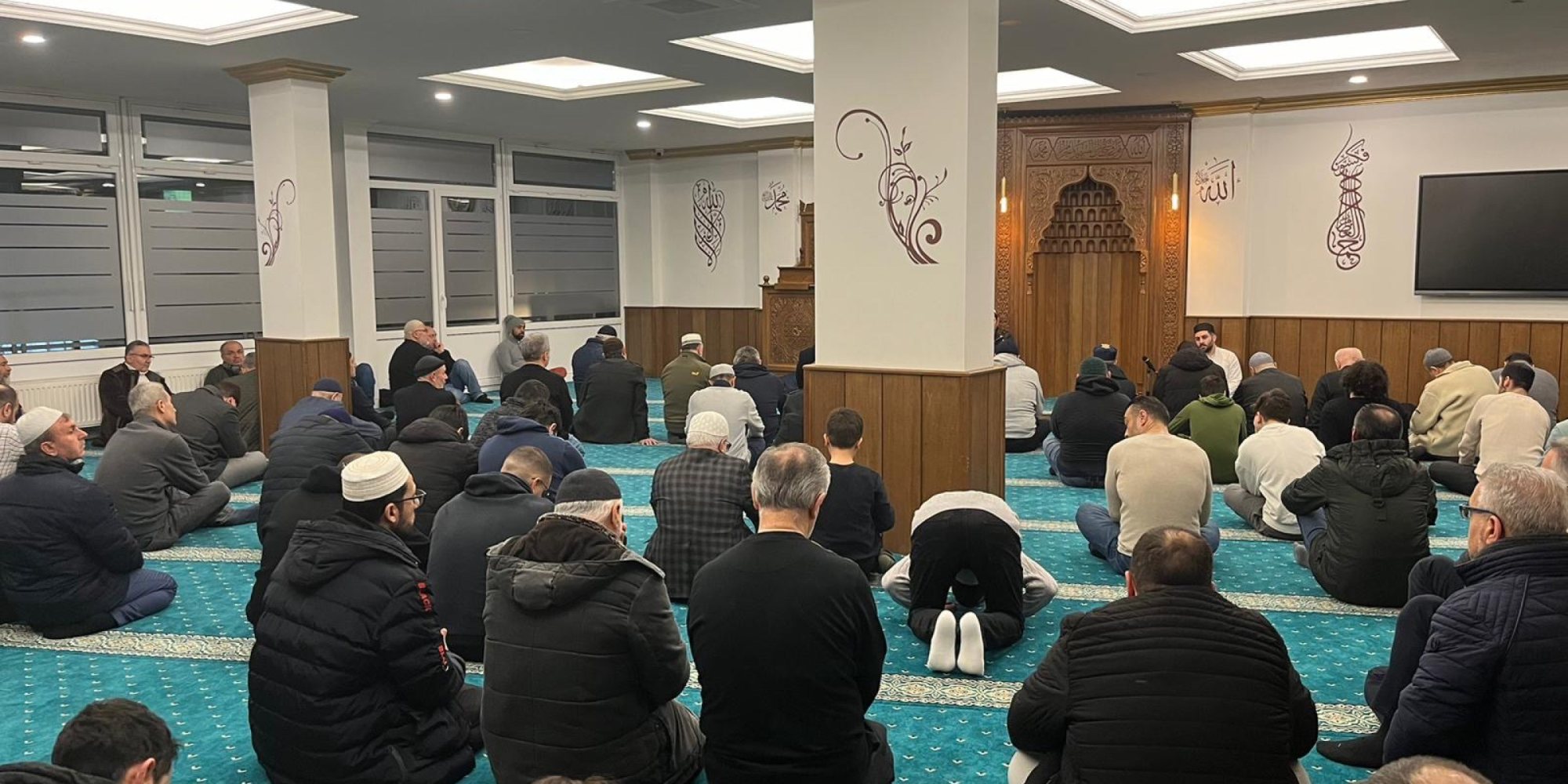 Gemeinde beim Festgebet in einer Moschee mit türkisem Teppich