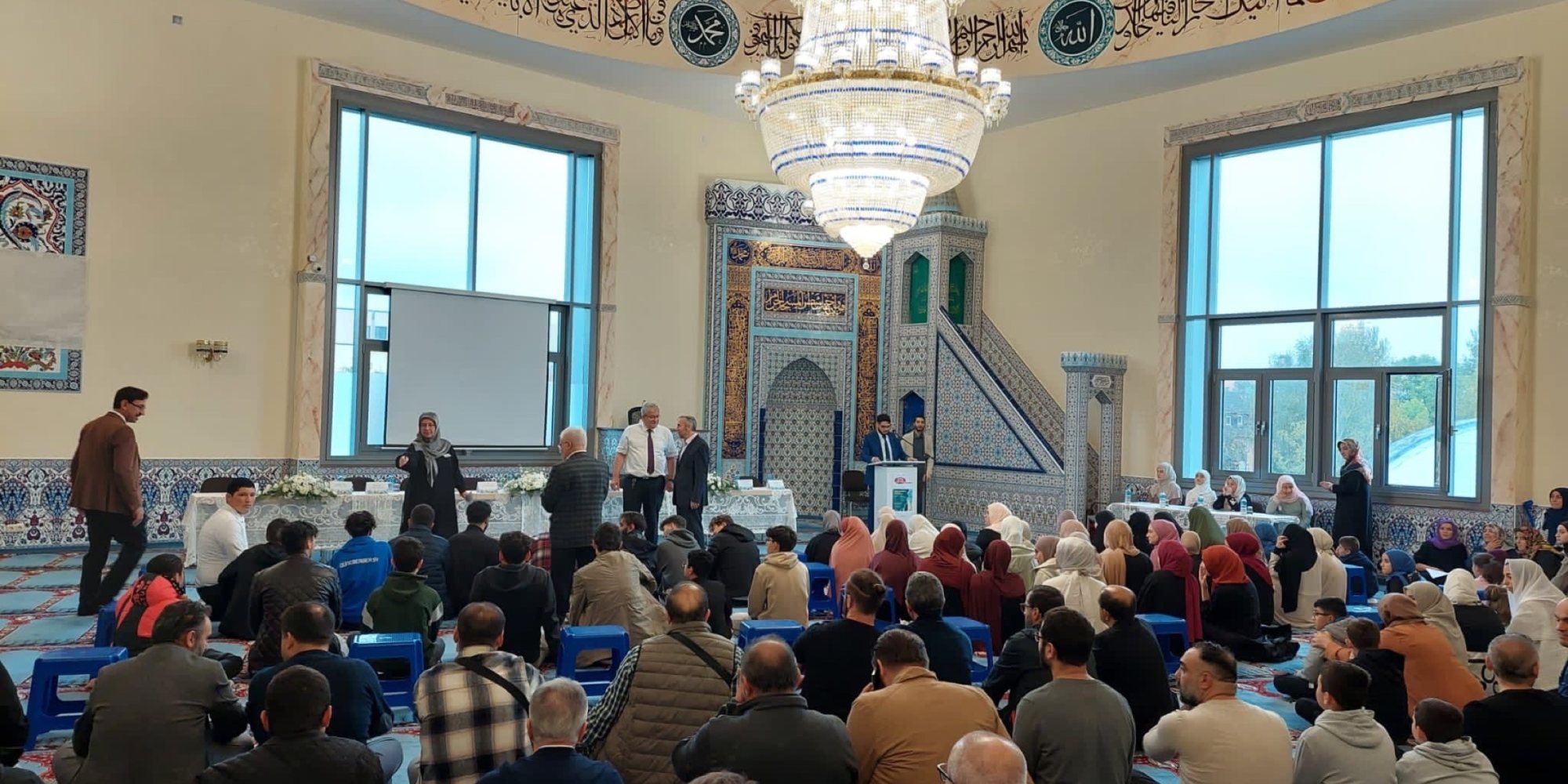 Innenraum einer Moschee mit Kuppel und Kronleuchter während einer Veranstaltung